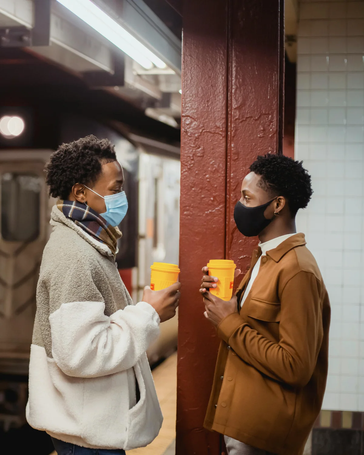 Two friends sharing coffee on a subway platform